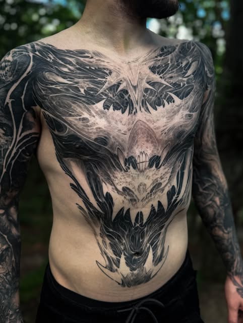 Symmetrical dark fantasy tattoo covering a client's chest and torso
